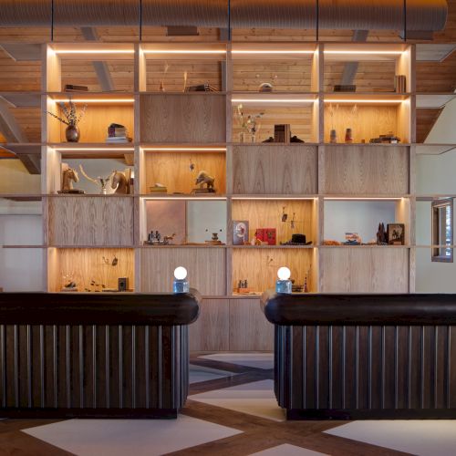 A stylish reception area with two dark, striped sofas facing a tall wooden shelving wall filled with decor and lighting accents, under warm lighting.