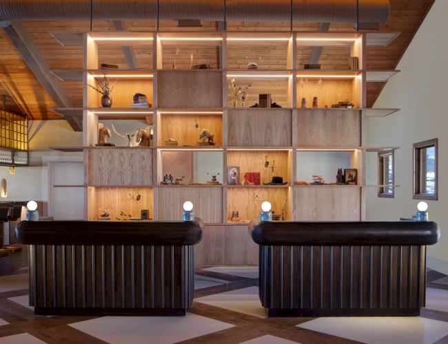 A stylish reception area with two dark, striped sofas facing a tall wooden shelving wall filled with decor and lighting accents, under warm lighting.