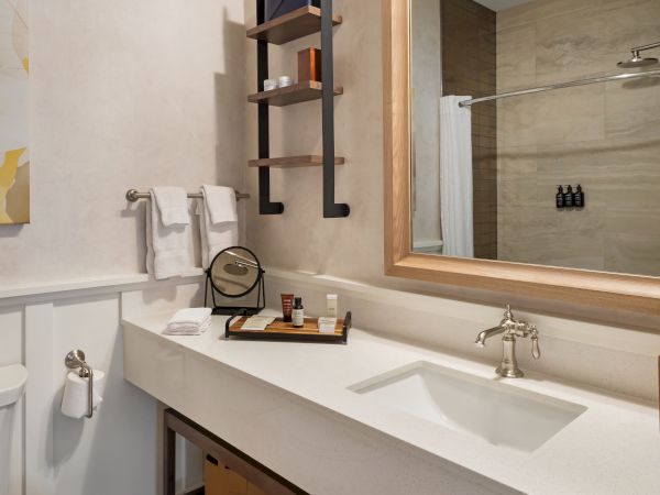 A modern bathroom with a sink, faucet, toiletries on a tray, towels, a mirror, and wall art. Neat and organized décor enhances the space.