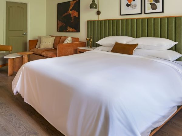 A cozy bedroom with a plush bed, orange couch, and stylish decor in warm, earthy tones, featuring framed art and soft lighting.