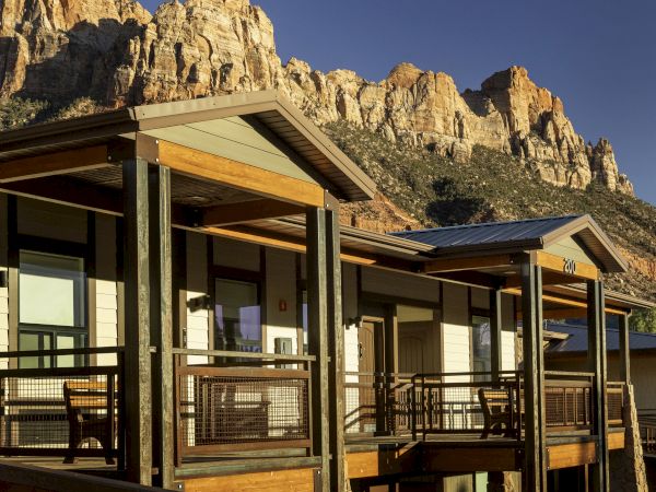 A modern building with balconies is set against a backdrop of rugged mountains and a clear blue sky.