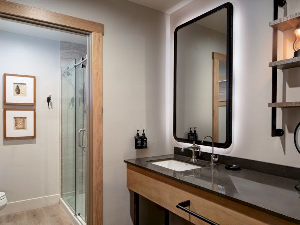 A modern bathroom with a double vanity, large mirror, and a glass-enclosed shower, plus wall shelves and framed art nearby. End.