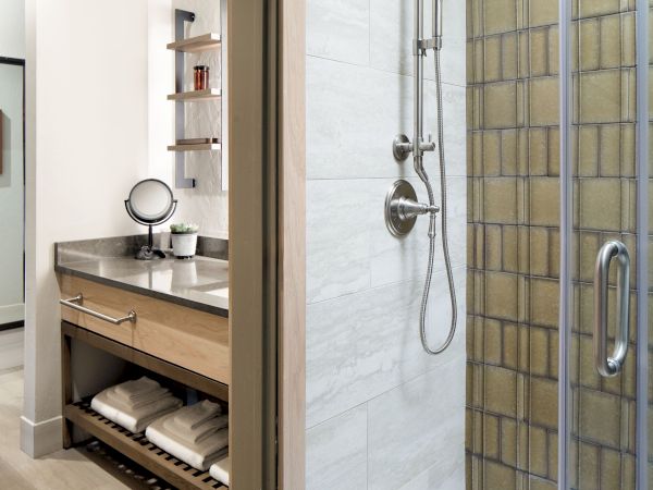 A modern bathroom with a glass shower door, vanity with a mirror, shelves, and folded towels below the counter.