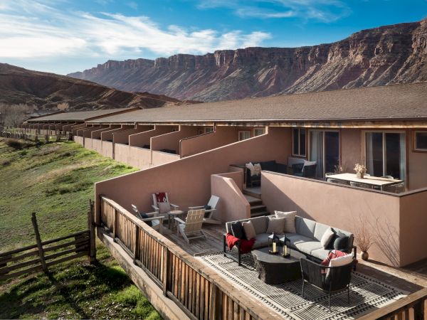 A row of beige townhouses with private balconies sits on a hillside patio, overlooking rugged mountains and a clear blue sky.