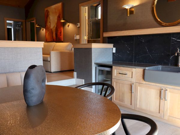 The image shows a modern interior with a round table, black vase, light wood cabinetry, and a gray couch in a tastefully decorated room.