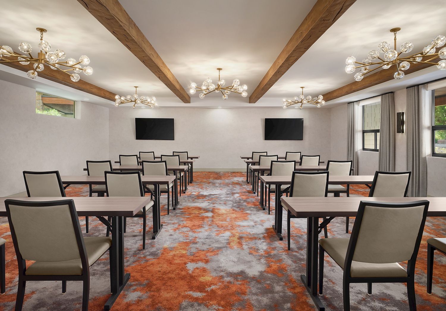 A conference room with tables, chairs, two screens on the wall, chandeliers, and a colorful carpet.