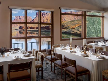 A cozy dining room with large windows showing a desert canyon view, set for a formal meal with white tablecloths and elegant place settings.