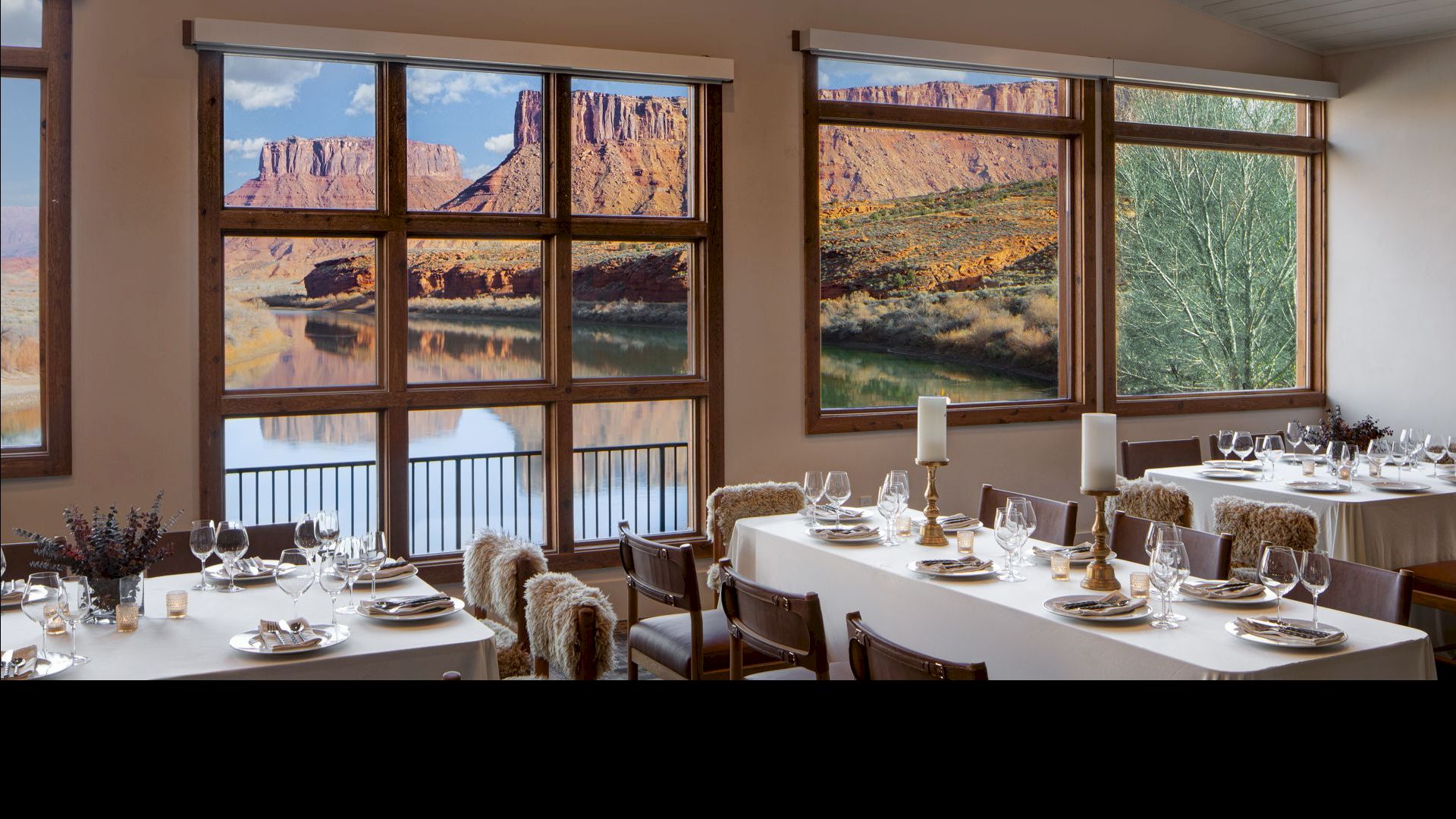 A dining room with white tablecloths, place settings, candles, and large windows overlooking a rocky canyon landscape outside. End.