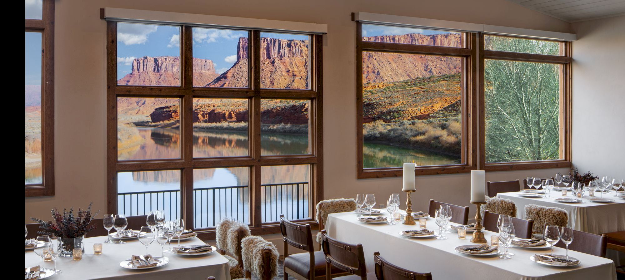 A dining room with white tablecloths, place settings, candles, and large windows overlooking a rocky canyon landscape outside. End.