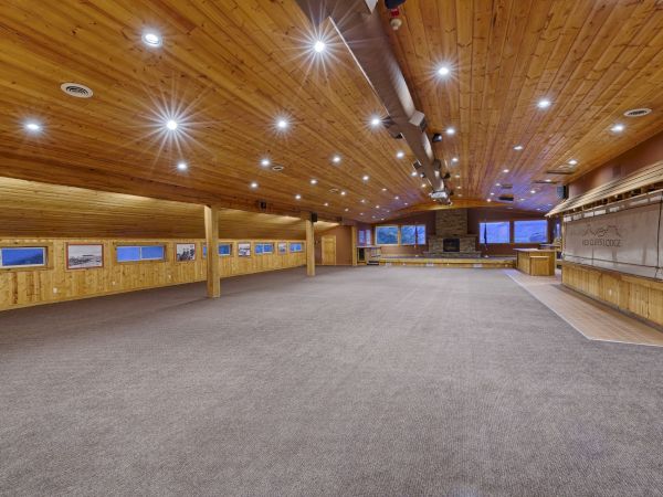 A spacious room with a wooden ceiling and carpeted floor, featuring a stage area and multiple lights overhead, ending the sentence.
