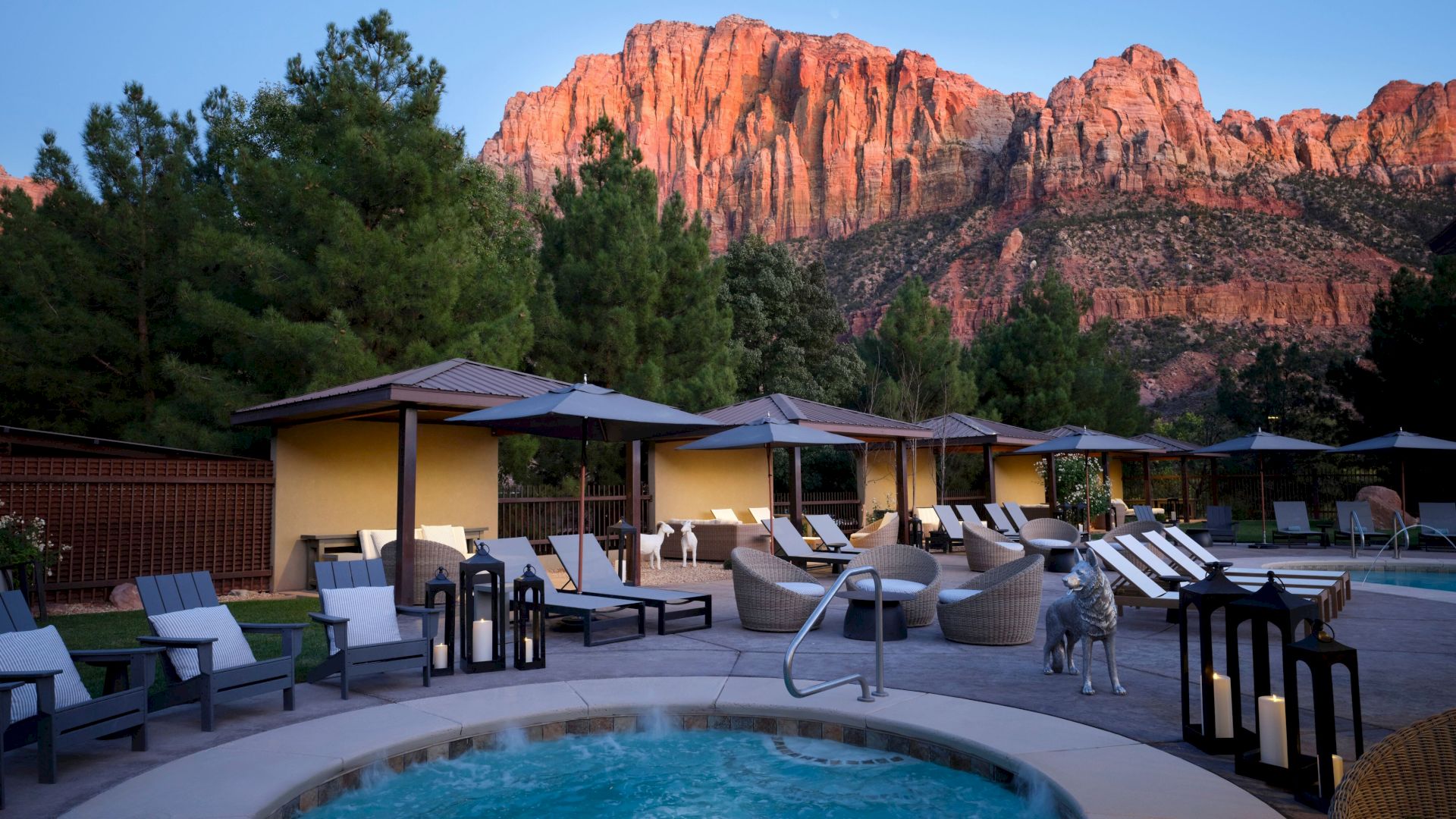 A luxurious outdoor pool area with lounge chairs and cabanas, set against a backdrop of majestic red mountains and lush greenery.