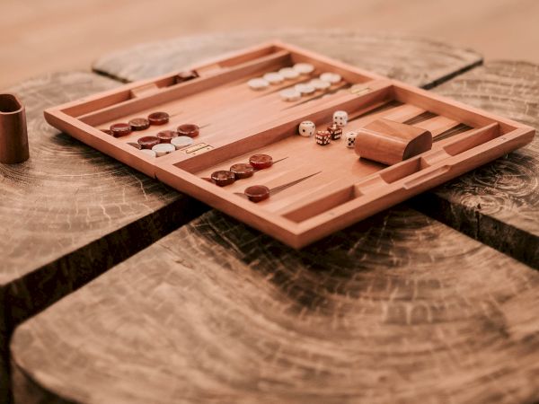 A blurred chic lounge with a wooden backgammon board on a rustic table, small wooden pieces scattered, cozy seating in the background, warm lighting.