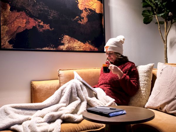 Woman sits on couch with blanket and tea