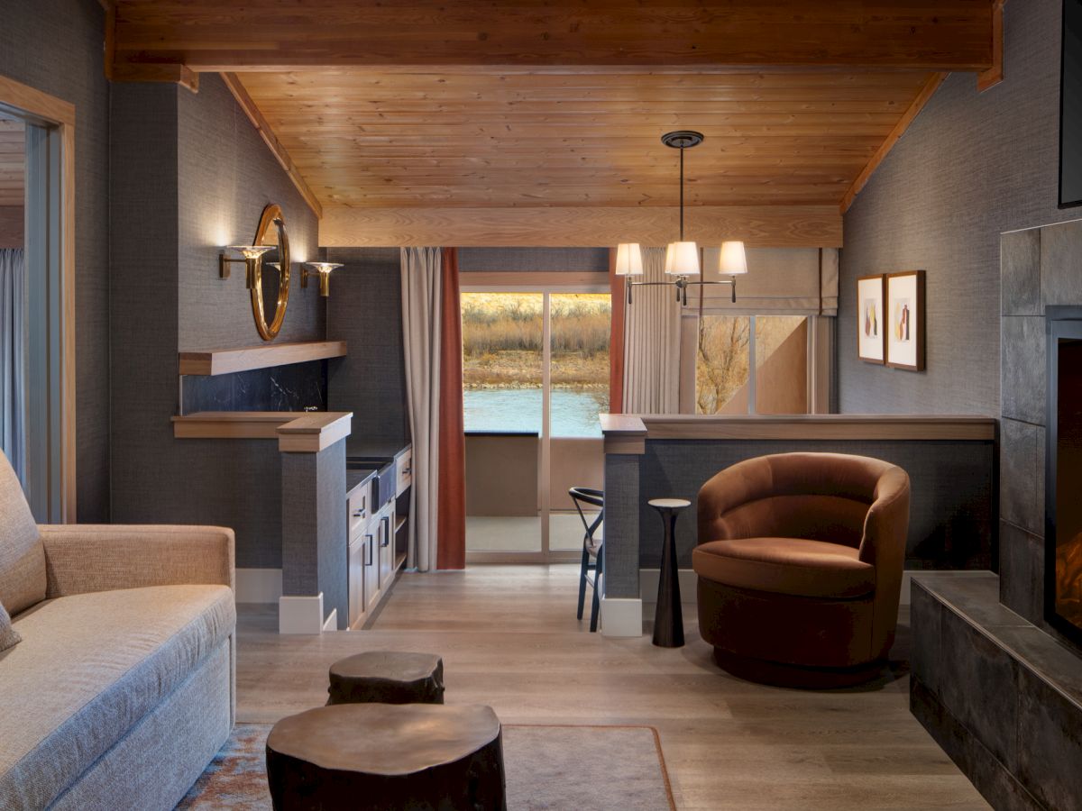 A cozy modern living space with a fireplace, sofa, armchair, TV, dining area, and large window views, all in warm wood tones.