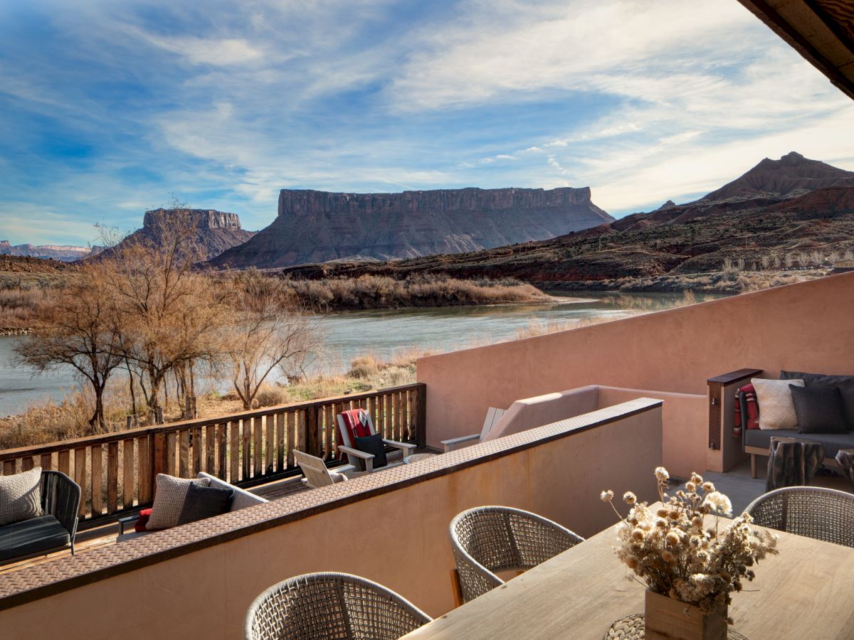 A terrace overlooks a desert landscape with Table Mountain-like mesas in the distance, a calm water body, and cozy seating on the patio.