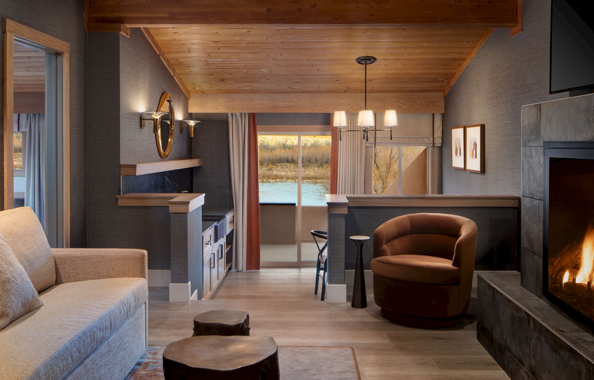 A cozy living room with a fireplace, sofa, round armchair, wood ceiling, bar-height seating, a windowed view, and warm ambient lighting. ending.