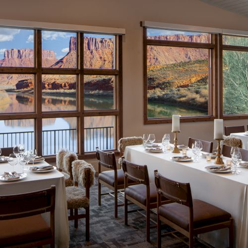A cozy dining room with large windows looking out at red rock formations; tables set for a formal meal with white tablecloths and glassware.