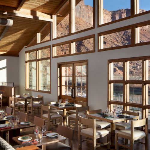 A cozy, modern restaurant interior with warm lighting, large windows, and wooden tables set for dining, creating a welcoming atmosphere.