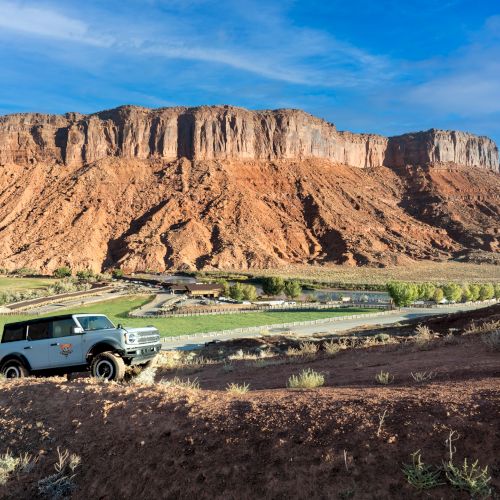 A desert landscape with red rock cliffs, a clear blue sky, and a winding river or stream at the base. Top it at 140 characters, always ending the sentence.