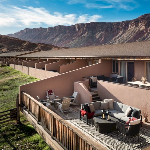 A hillside resort with beige balconies and a row of outdoor seating, scenic desert mountains in the background, sunny day.