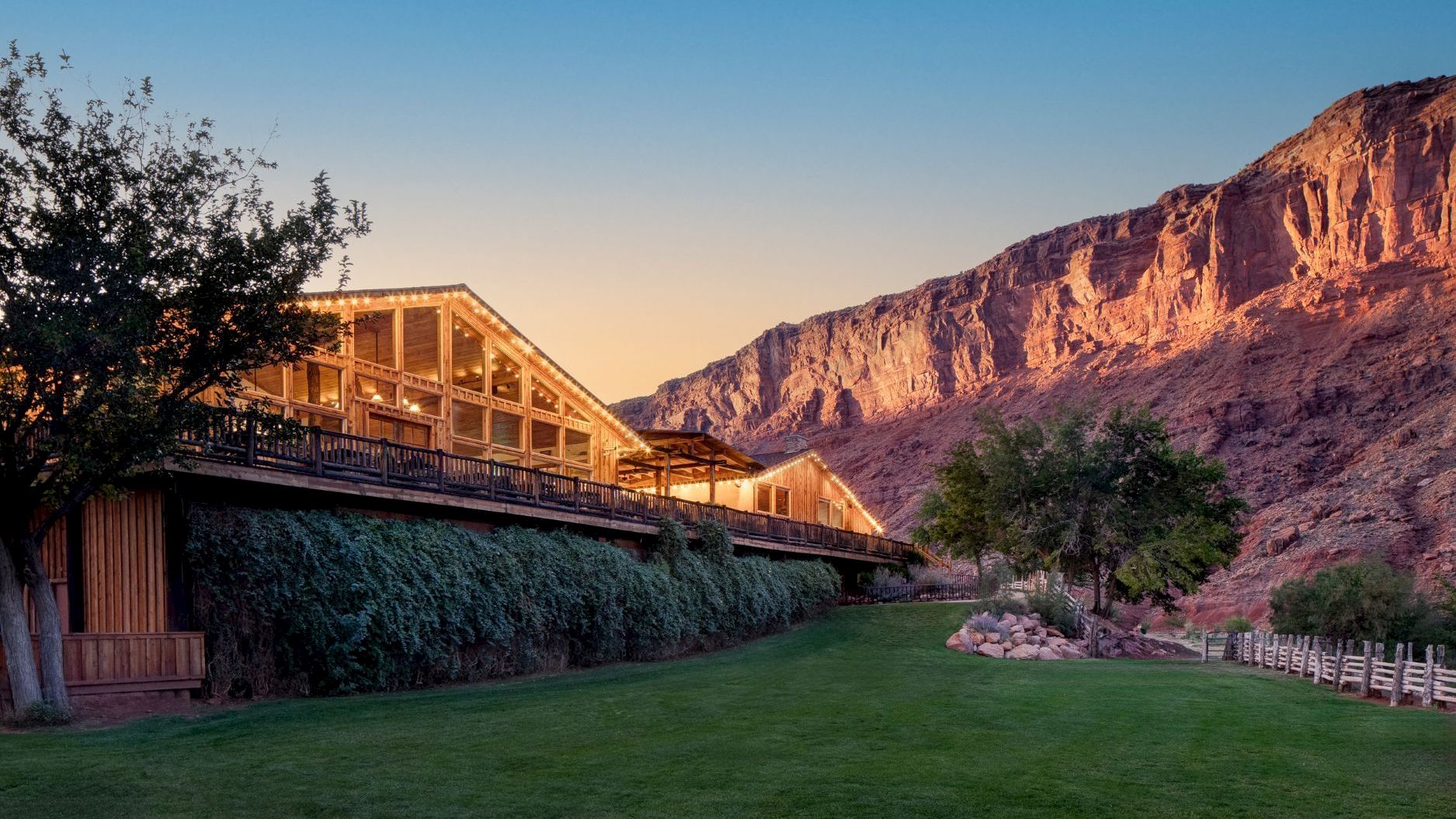 A picturesque landscape with a wooden building, lush greenery, and a mountain backdrop at sunset, creating a serene and scenic view.