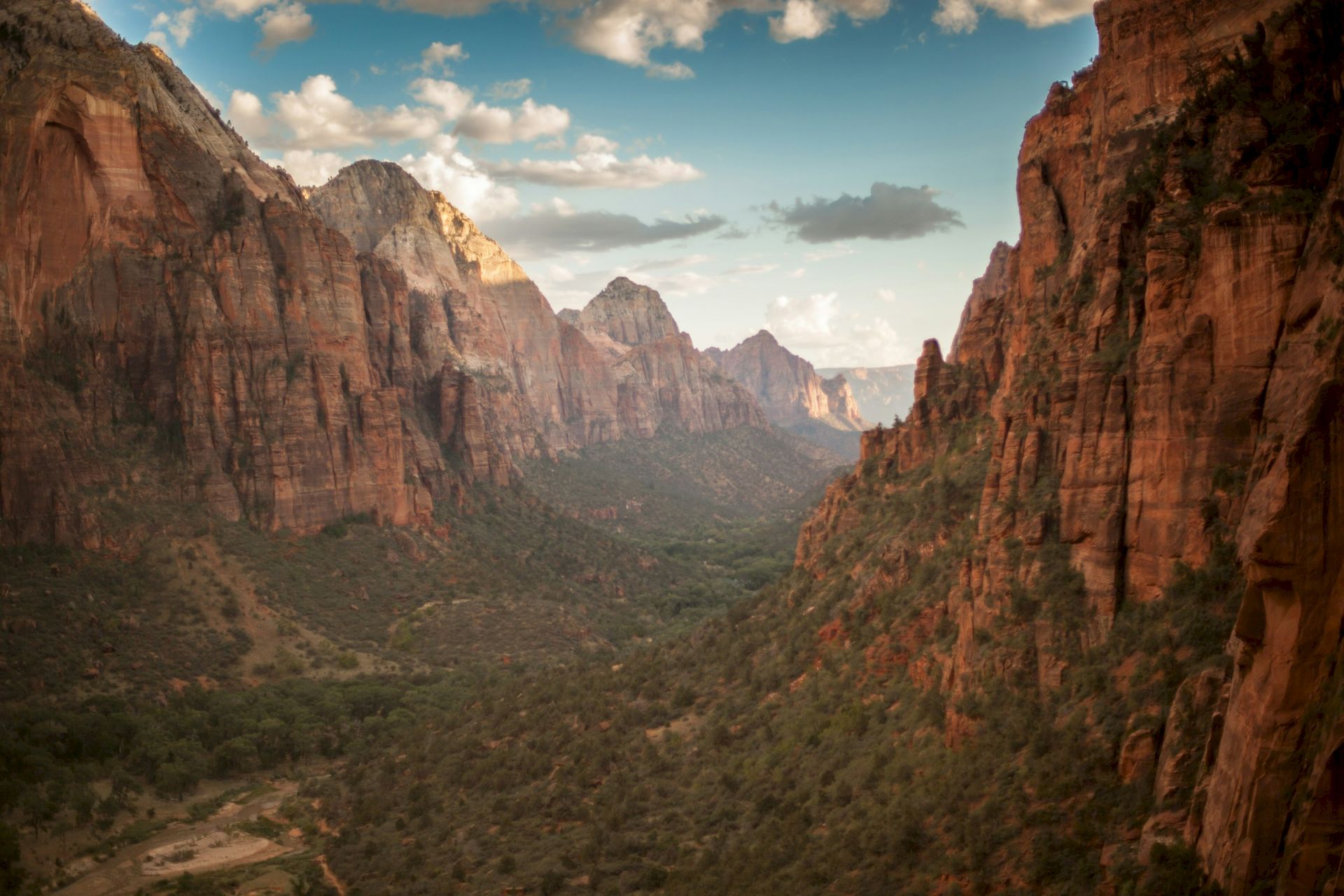 The image shows a canyon landscape with red rock formations, a green valley, and a partly cloudy sky.