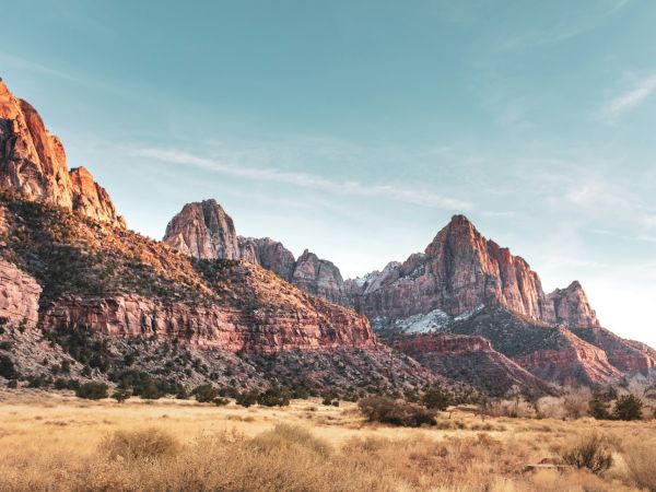 The image shows a scenic landscape with rugged mountains, rocky cliffs, and a grassy field under a clear blue sky.