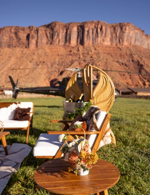 Outdoor seating with chairs and a table on grass, decorated with flowers. A desert mountain landscape is in the background.