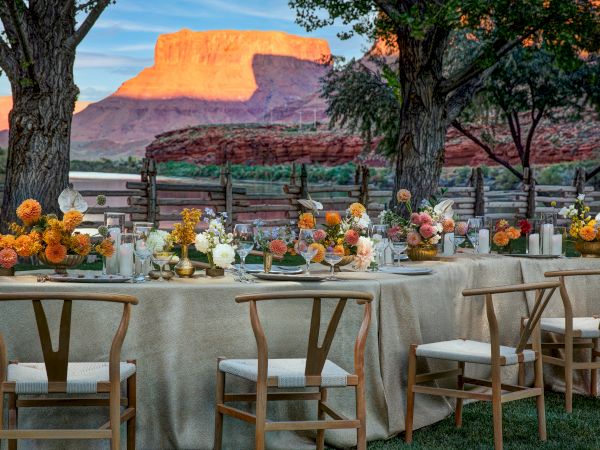 An outdoor dining setup with elegantly arranged tables and chairs, vibrant floral centerpieces, overlooking a scenic mountainous landscape.