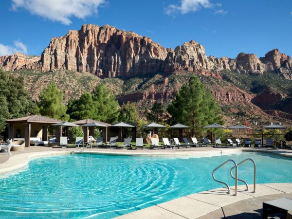 A serene pool with lounge chairs, cabanas, and a stunning mountain range in the background under a clear blue sky.