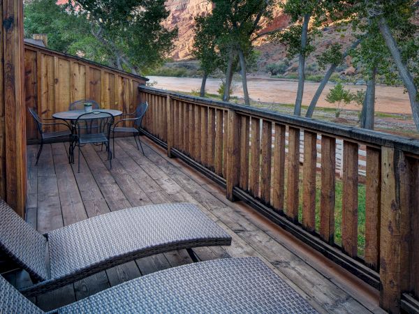 A wooden deck with two lounge chairs, a small table, and chairs overlooking a river and trees in a serene natural setting.