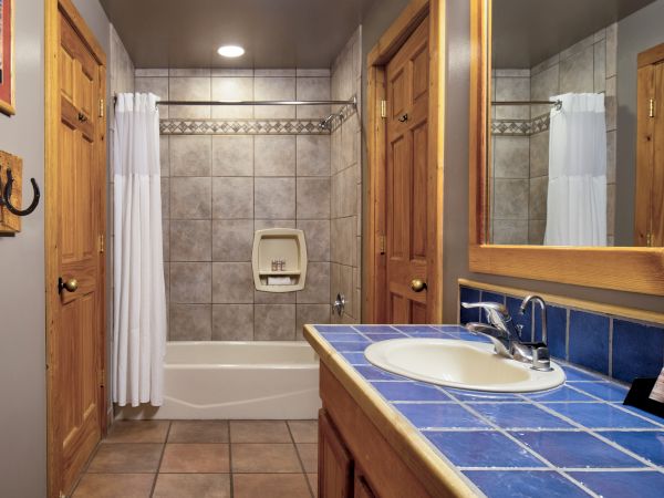 A bathroom with a tiled shower and curtain, wooden door, blue-tiled sink counter, mirror, and hooks on the wall.