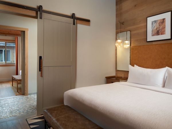 A modern hotel room with a large bed, sliding barn door, and a view into a bright entry area.