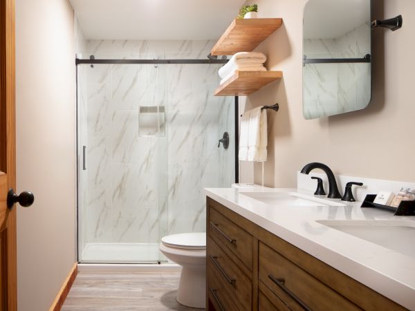 A modern bathroom featuring a glass shower, wood vanity with dual sinks, shelves with towels, and a mirror.
