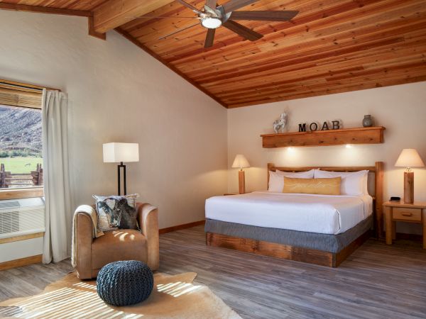 A cozy bedroom with a wooden ceiling, double bed, and armchair. The room has a window, lamps, and decor spelling "MOAB".