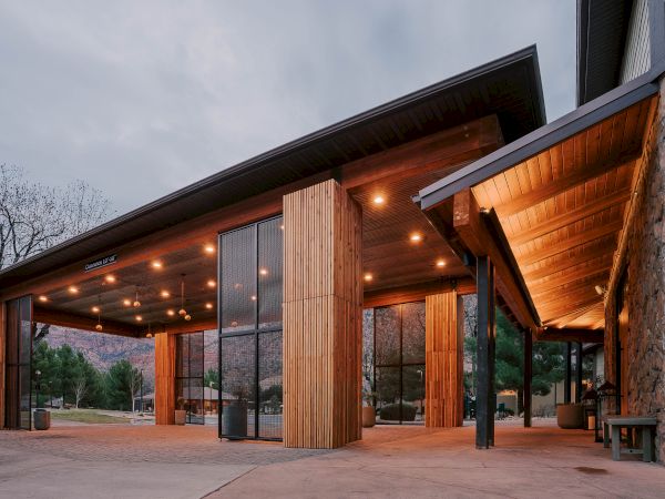 A modern building with tall wooden columns, warm lighting, and stone accents under a covered entrance&mdash;looks inviting and rustic.